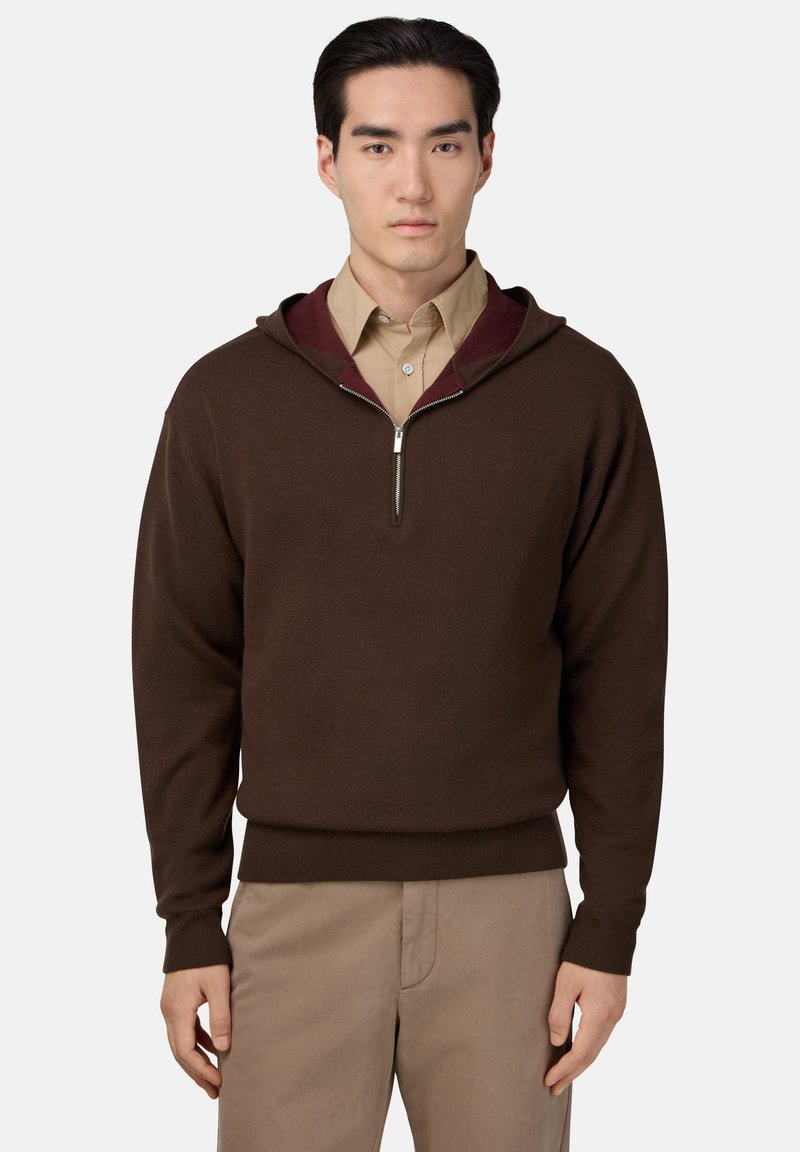 Hnedá mikina na zips s burgunďskou podšívkou kapucne, pletená textúra, rebrované manžety a lem. Nosená cez svetlohnedú košeľu s golierom.