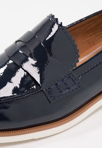 Mocassin en cuir bleu foncé brillant avec détail de bord en zigzag et semelle contrastée marron et blanche, coutures visibles et bride penny.
