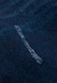 Texture de tissu en denim bleu foncé avec une ligne de couture bleu clair distincte courant verticalement, mettant en valeur le tissage et la finition du matériau.