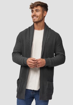 Mörkgrå stickad cardigan med sjalkrage, ribbade manschetter och två framfickor. Bärs över en ljus skjorta och ihop med blå jeans.