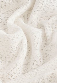 Tissu en dentelle blanche avec un motif en maille ouverte intricate, présentant une texture douce et une apparence légère. Les bords sont légèrement effilochés.