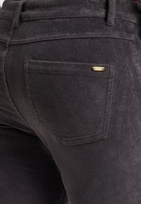 Donkergrijze corduroy broek met een geweven stof, subtiele ribbels en een klein goudkleurig accent op de achterzak.