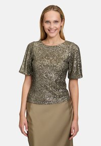 Bluzka z krótkim rękawem i okrągłym dekoltem o teksturowej powierzchni pokrytej złotymi cekinami, zestawiona z gładką, w neutralnym kolorze spódnicą.