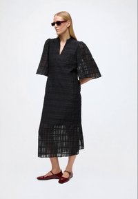 Vestido midi preto com decote em V, mangas bufantes, tecido texturizado, painéis semi-transparentes e silhueta reta, combinado com sapatilhas bordeaux.