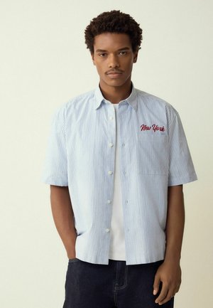 Kurzärmeliges Hemd mit Knöpfen in hellblau-weißen Streifen, mit einem roten "New York"-Stickereimotiv auf der Brusttasche.