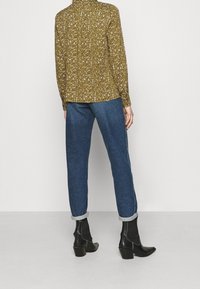 Oliven grøn bluse med et struktureret mønster, parret med lyseblå jeans rullet op ved blusserne og sorte ankelstøvler med blokhæle.