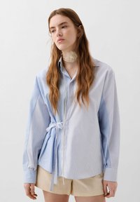 Blauw-wit gestreepte overhemd met lange mouwen, gestrikt in de taille, met een kraag en een textuuraccent rond de hals.