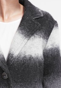 Blazer de mezcla de lana en degradado de negro a gris con un acabado texturizado, solapas de pico y cierre de un solo botón, con un sutil detalle de bolsillo.