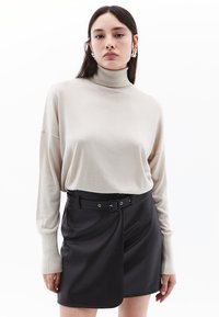 Beige kaulusneule, jossa on pitkät, löyhät hihat, yhdistettynä mustaan, keinotekoiseen nahkahameeseen, jossa on vyö ja napitussuljin. Teksturoidut materiaalit.
