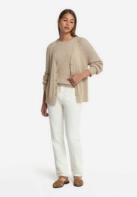 Beige cardigan med texturerade ärmar, i kombination med en ljusbeige topp och vita byxor. Bruna sandaler fulländar outfiten. Enkel och avslappnad design.