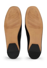 Semelles de chaussures habillées en cuir noir avec sections de talons en caoutchouc beige et noir, présentant des motifs de rainures diagonales et un embossage de marque visible.