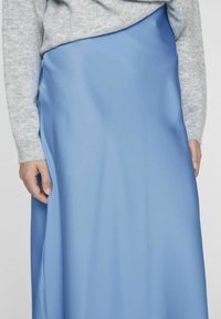 Svetlo modra satenasta krila z gladko teksturo, zložljivim dizajnom in stranskim razpokom. V kombinaciji z sivo pleteno majico.