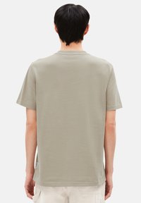 Helles olivengrün, kurzärmliges T-Shirt aus weicher Baumwolle mit Rundhalsausschnitt und geradem Schnitt, versehen mit einem kleinen Logopatch am Saum.