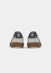Adidas sneakers med en øverdel i grå sælskinds, sorte accenter, blå hælflap og en struktureret brun gummisål. Hvide detaljer på hælen.