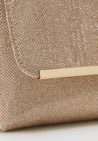 Sac à main doré métallique avec un tissu métallique texturé, présentant une barre d'accent dorée lisse sur la poche avant.