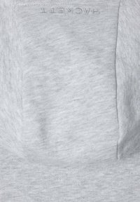 Felpa grigia con una texture liscia, dotata di una tasca a marsupio e un logo ricamato discreto vicino al colletto. Design morbido e informale.
