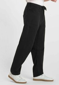 Zwarte cargo pants met een losse pasvorm, voorzien van een trekkoord in de taille, zij- en achterzakken, en een gladde katoenstructuur. Gecombineerd met witte sneakers.