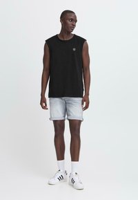 Svart ermeløs skjorte, lyse denimshorts, hvite sneakers med svarte striper, stående posisjon. Enkelt design, avslappet passform, minimalt med detaljer.