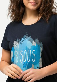 Navyblauwe katoenen T-shirt met een blauw abstract penseelstrekenontwerp en het woord "BISOUS" in witte tekst op de voorkant. Korte mouwen.