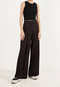 Mustaa leveälahkeista housua punaisilla pilkuilla, joissa on teksturoitu kangas, yhdistetty tiukkaan mustaan ilman hihoja toppiin ja mustiin lenkkareihin.