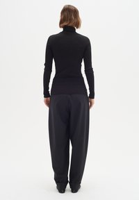 Schwarzer gerippter Rollkragenpullover, kombiniert mit lässig sitzenden schwarzen Hose, die eine glatte Textur und eine gerade Silhouette aufweist.