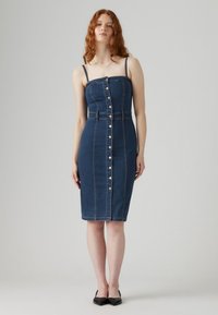 Vestido de mezclilla en azul oscuro con forma ajustada, tirantes finos, botones en el frente y cintura ceñida. Textura suave y diseño a la altura de la rodilla.
