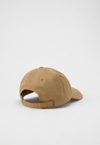 Brown cotton baseball cap with a curved brim, adjustable strap, and ventilated eyelets on the back for breathability.