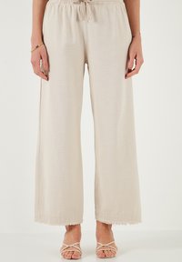 Hellbeige weite Hose mit elastischem Bund und Kordelzug. Verfügt über Fransenverzierungen am Saum und einen glatten, strukturierten Stoff.