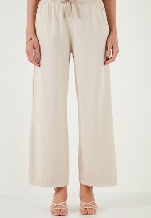 Hellbeige weite Hose mit elastischem Bund und Kordelzug. Verfügt über Fransenverzierungen am Saum und einen glatten, strukturierten Stoff.