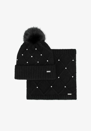 Gorro de punto negro con pompones de piel y patrón de diamantes, adornado con pequeñas cuentas blancas, acompañado de una bufanda negra a juego.