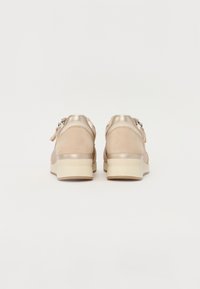 Beige tenisky s hladkým koženým a semišovým povrchem. Polstrovaná pata a texturovaná podrážka. Obsahuje zipové zapínání a metalické akcenty.