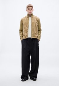 Tumepruun seemisnahast bomberjakk soonikkoeliste varrukatega, kombineeritud suures suuruses mustade pükstega. Modell kannab all heledat kudumit.