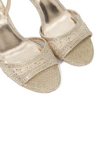 Beige hoge hakken sandalen met sprankelende versieringen, met een textiele bovenkant en open teen ontwerp, die decoratieve details accentueren.