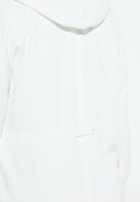 Bílá mikina s kapucí, vyrobená z jemného materiálu, s nenápadným švem. Obsahuje stahovací šňůrku vzadu pro úpravu.