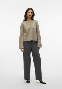 Beżowy sweter w splot kablowy z szerokimi rękawami w połączeniu z szarymi spodniami o wysokim stanie i szpiczastymi burgundowymi szpilkami. Prosty, teksturowany wzór.