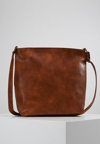 Brun læder crossbody taske med justerbar rem, glat tekstur og minimalistisk design placeret på en hvid pedestal mod en grå baggrund.