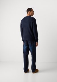 Navy ribbed sweater with round neck, paired with dark blue jeans, and brown slip-on shoes. Minimalist design, soft texture, and relaxed fit.