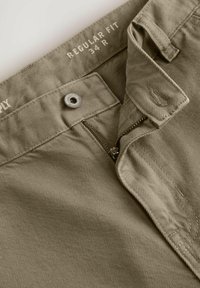 Pantalons kaki ajustement régulier, avec une fermeture éclair, bouton en métal et une texture lisse avec des détails de couture visibles. Taille 34 R.
