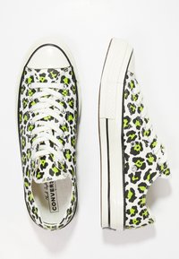 Trampki z nadrukiem w panterkę na płótnie z neonowymi zielonymi i czarnymi akcentami, biała gumowa podeszwa i metalowe oczka, z białymi sznurówkami i czubkiem.