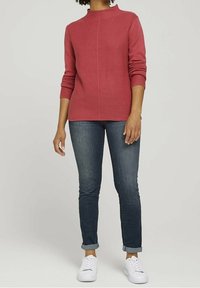 Pink knit sweater with a high neckline, long sleeves, and a textured pattern, paired with dark jeans and white sneakers.