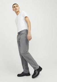 Jean en denim gris à coupe décontractée, design à cinq poches et couture contrastée. Associé à un t-shirt blanc uni et des chaussures noires.