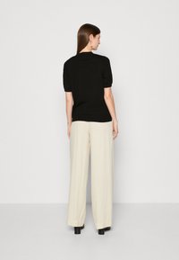 Top scurt negru cu guler rotund, asortat cu pantaloni largi de culoare crem. Finisaj din material neted, cu o croială relaxată.