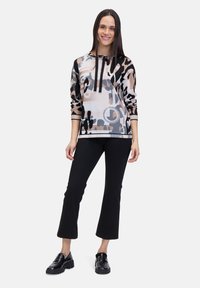 Hooded pullover in a lightweight fabric, featuring a muted animal print in beige, black, and blue, paired with black cropped pants and chunky shoes.
