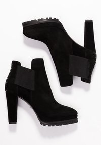 Černé semišové kotníkové boty na vysokém podpatku, s elastickými bočními panely a hřebíčkovými akcenty kolem kotníku. Texturovaná gumová podrážka pro lepší přilnavost.