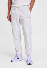 Helle graue Jogginghose aus weichem Stoff, mit einem elastischen Bund und Kordelzug, sowie einem kleinen roten Logo auf dem linken Oberschenkel.