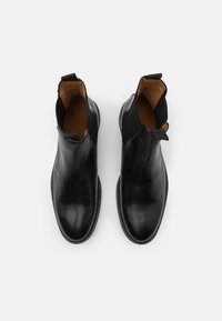 Botas de tobillo de cuero negro con paneles elásticos a los lados, puntera redondeada y detalles de costura mínimos. El interior cuenta con un forro de cuero marrón y tiradores.