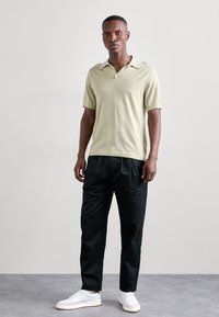 Lysegrønn kortermet polo skjorte, kombinert med svarte plisserte bukser og hvite joggesko. Glatt tekstur, klassisk kragedesign.