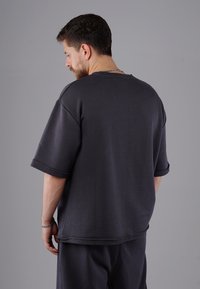 Dunkelgraues, übergroßes T-Shirt mit Rundhalsausschnitt, kurzen Ärmeln und umgeschlagenen Bündchen. Hergestellt aus einem weichen Stoff mit glatter Textur.