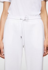 Vita sweatpants med dragsko i midjan, som har en slät yta och silverfärgade metallaccent på snörena och logotypen.