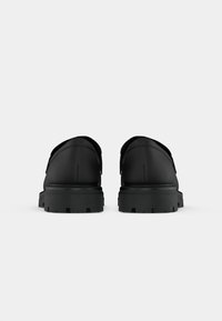 Fekete cipők sima felülettel, párnázott gallérral és texturált gumitalppal, melyek mély barázdákkal rendelkeznek a tapadásért. Minimalista design, díszítések nélkül.
